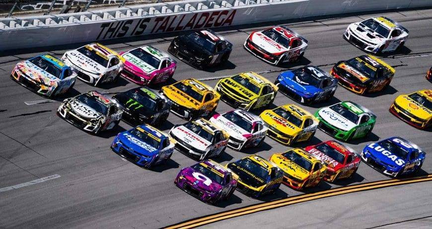 NASCAR cars are lined up on the track, ready for the race, showcasing their vibrant colors and sponsor logos.