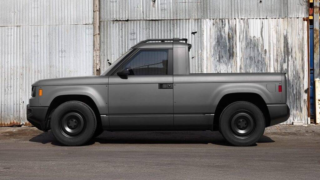 027 Slate Truck EV parked in an outdoor setting, showcasing its compact design with unpainted gray composite body panels, a five-foot bed, and a digital gauge cluster visible through the windshield. The truck features a minimalist aesthetic, emphasizing its customizable accessories and practical features.